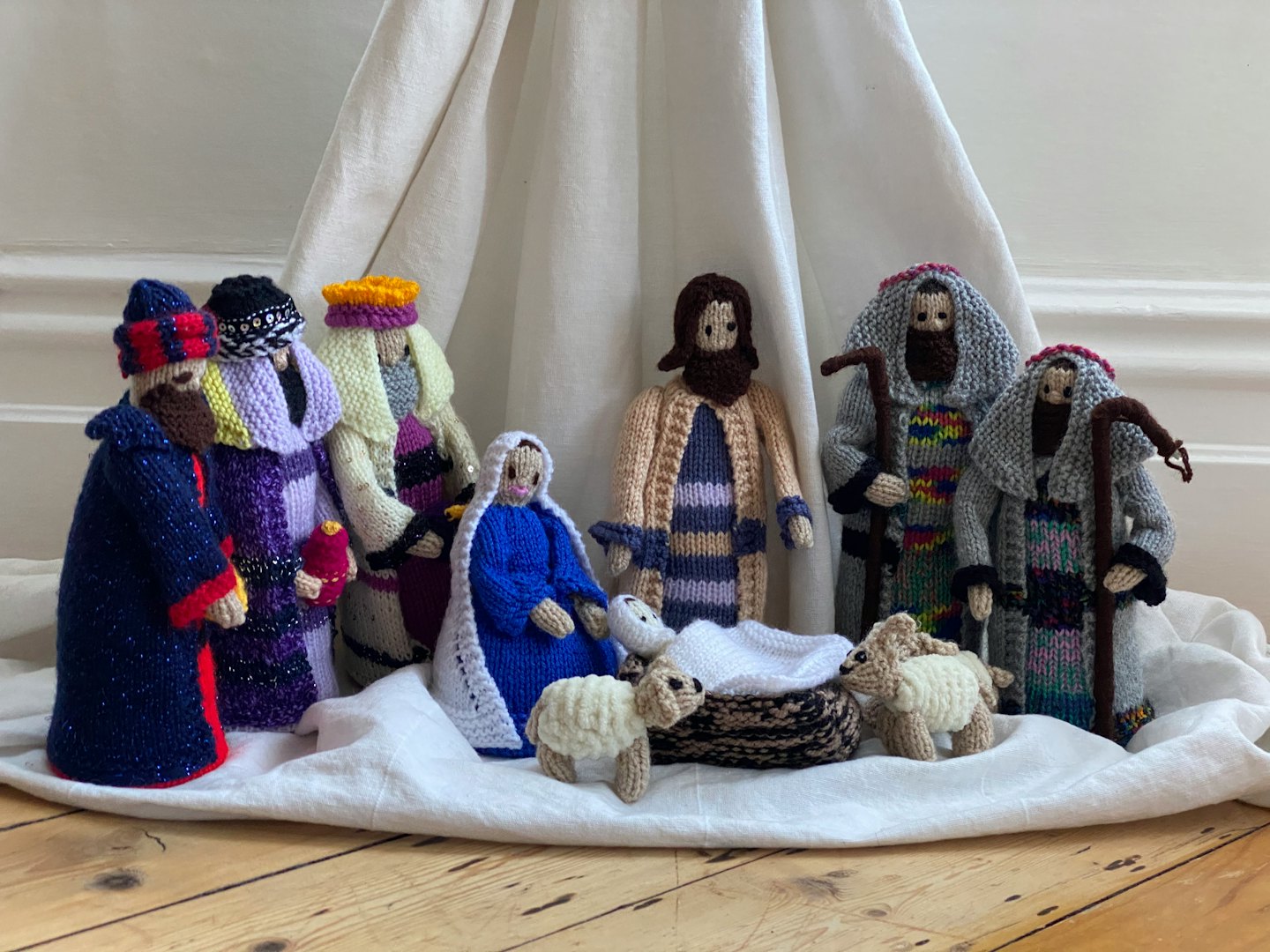 Presepe fatto a mano con figure colorate su stoffa bianca.